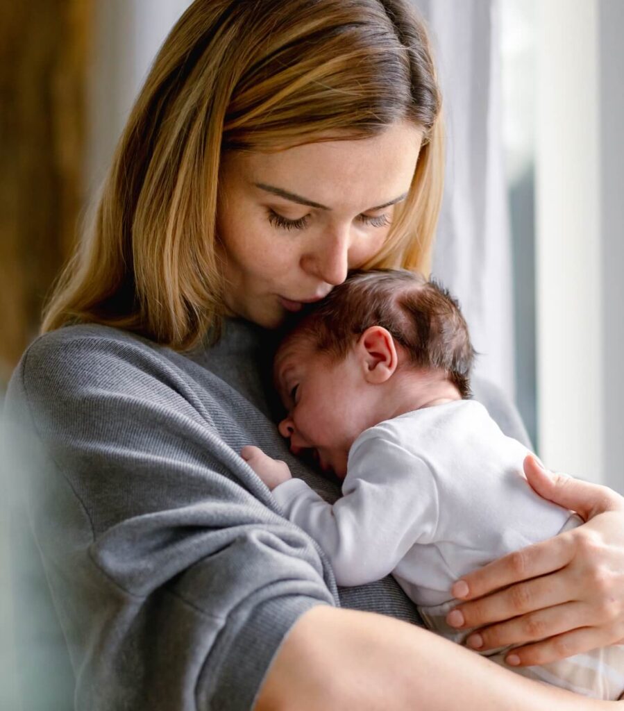 mother holds the baby in her arms and kisses the top of the head