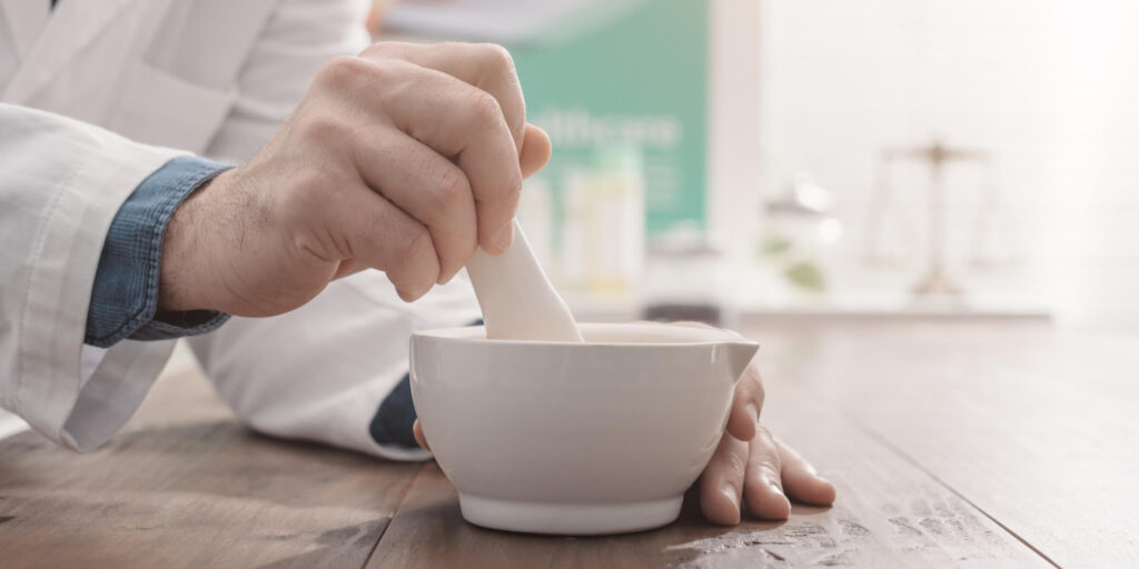 closeup of man in lab coat using a mortar and pestle.