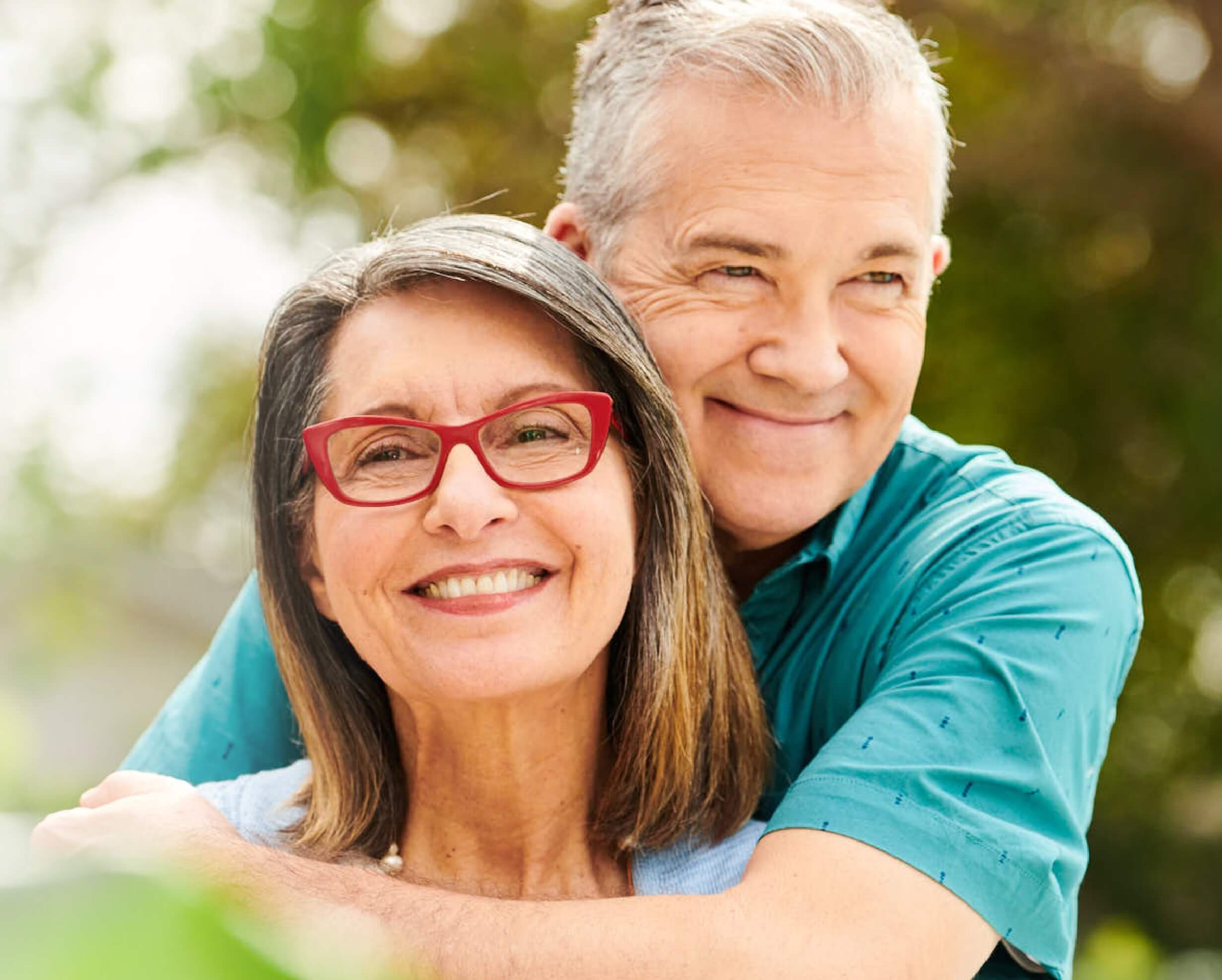 a man hugs a woman in red glasses. both are smiling