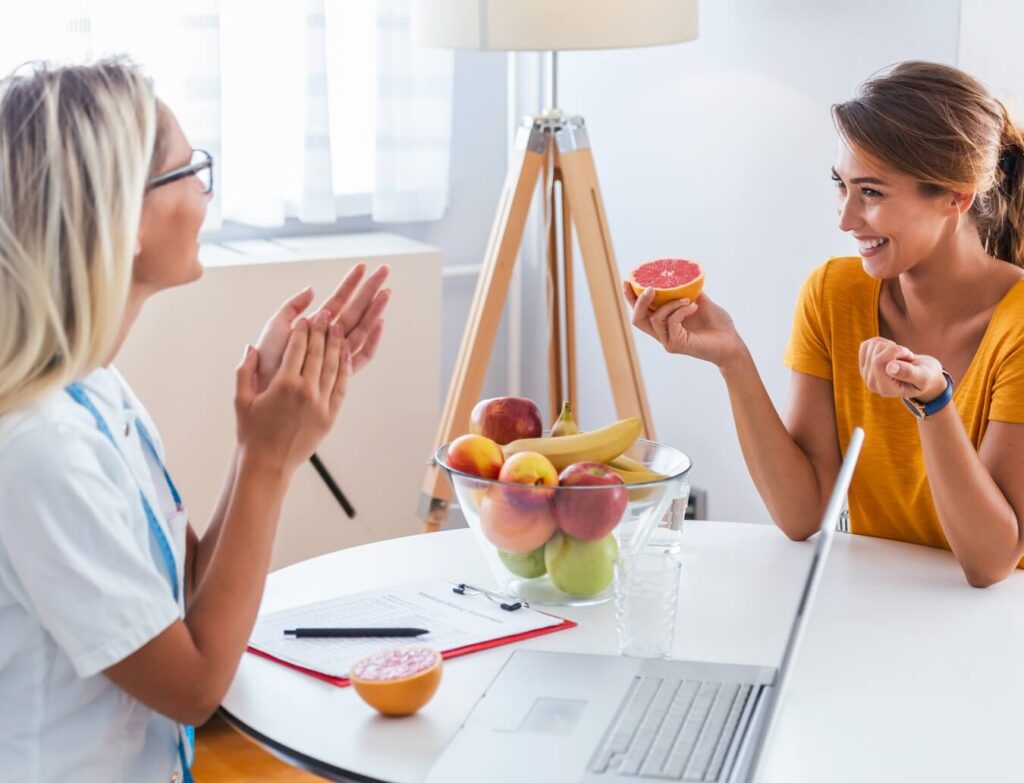 a medical worker and a woman are talking at the table. on the table between them are a pen and a questionnaire, a laptop, a glass
